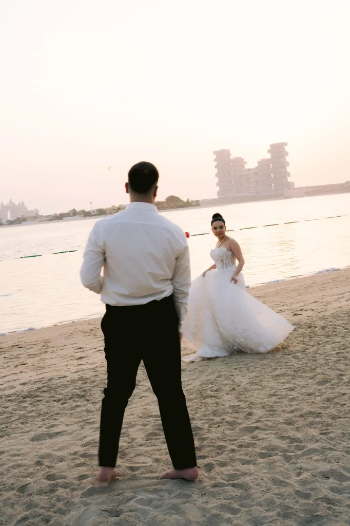 Groom watching the bride walk along the beach at sunset