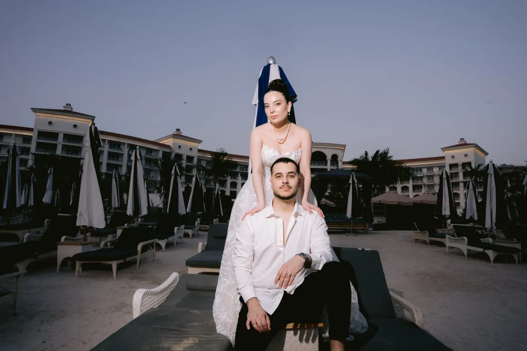 Bride sitting on the groom’s shoulders by a hotel pool at dusk