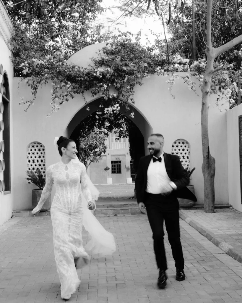 Black and white photo of the bride and groom walking through a courtyard