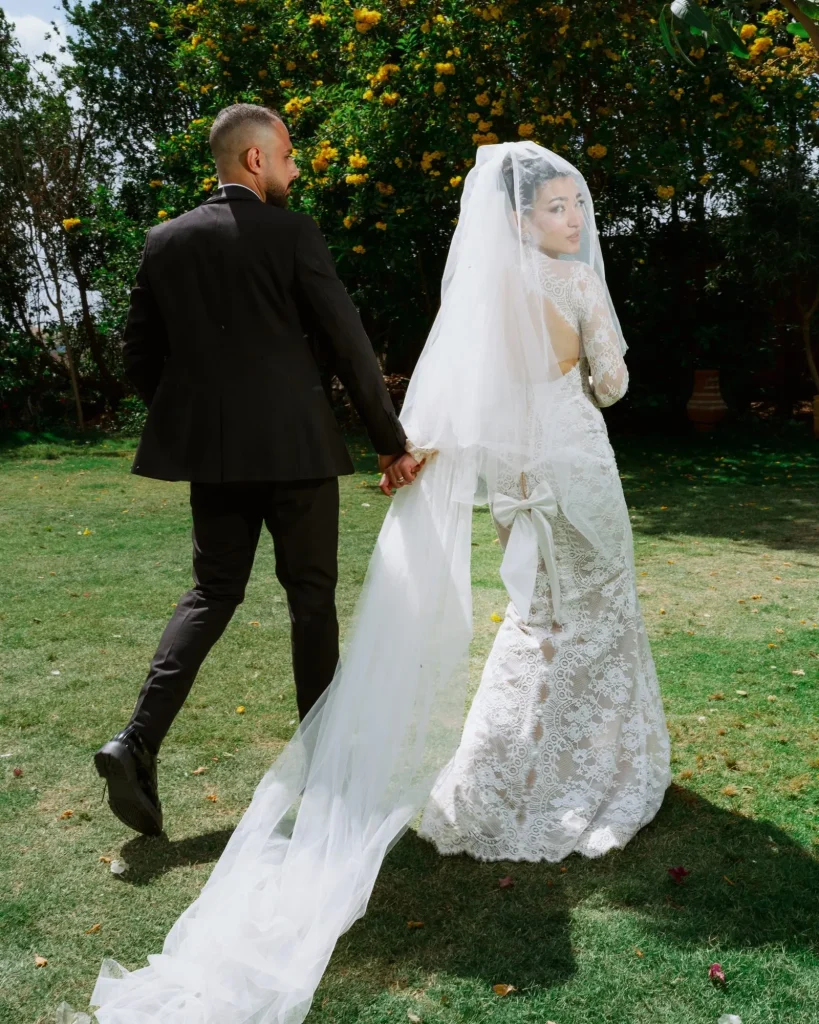 Bride and groom walking hand in hand across a garden lawn