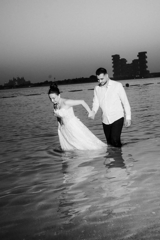 Black and white photo of a bride and groom walking hand in hand through the sea