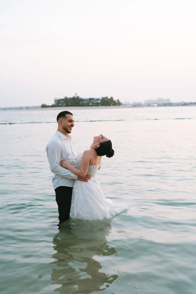 Bride and groom laughing together while standing in the sea