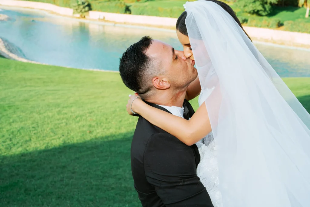 Groom kissing the bride beside a lake on a green lawn